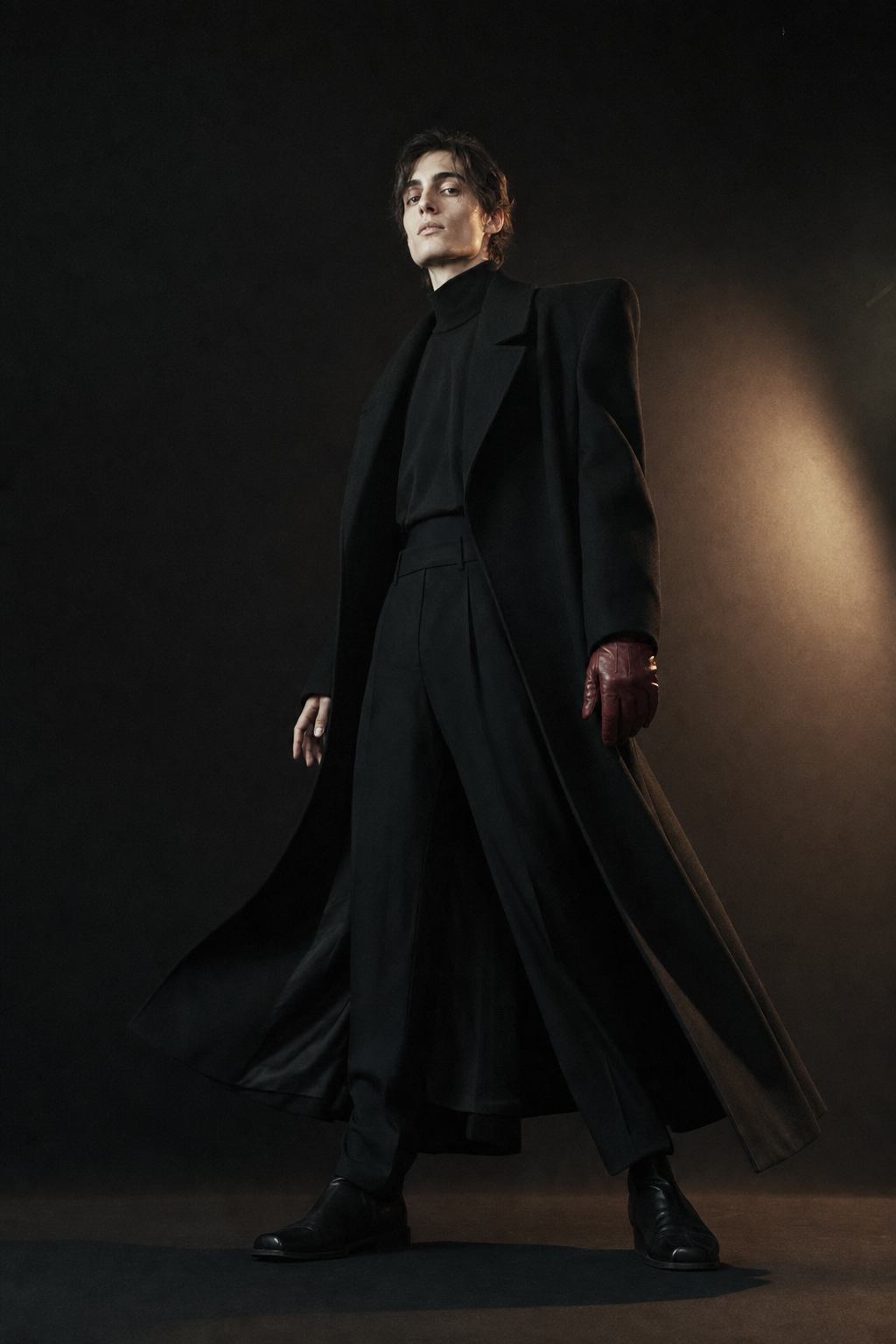 Androgynous adult model in a sculptural black coat, photographed from a low angle